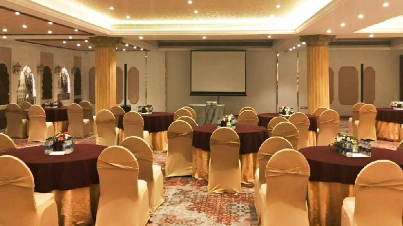 An image of a warmly lit event hall with chairs, round tables, and a projector - Kaldan Samudra Palace